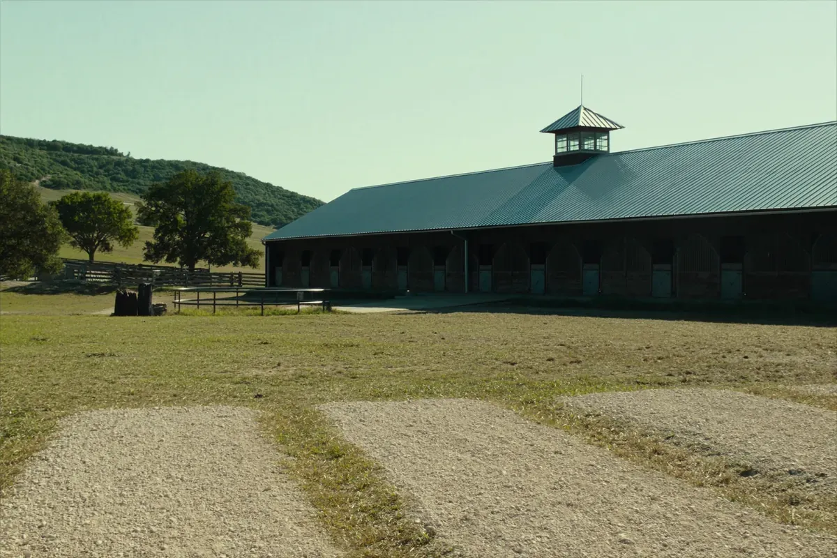 A long horse stable with a metal roof and cupola on Hill Country pasture