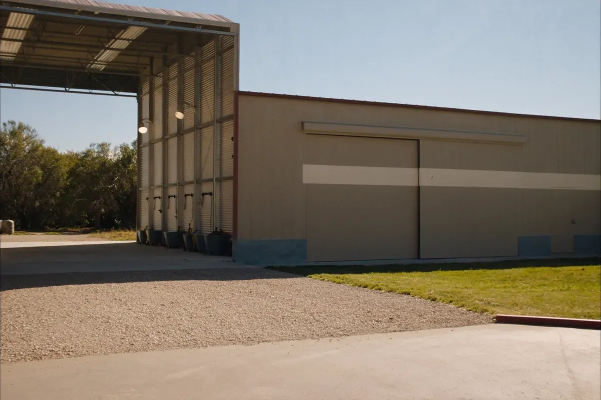 A metal pole barn with an open equipment canopy and a sliding-door bay in the Texas Hill Country