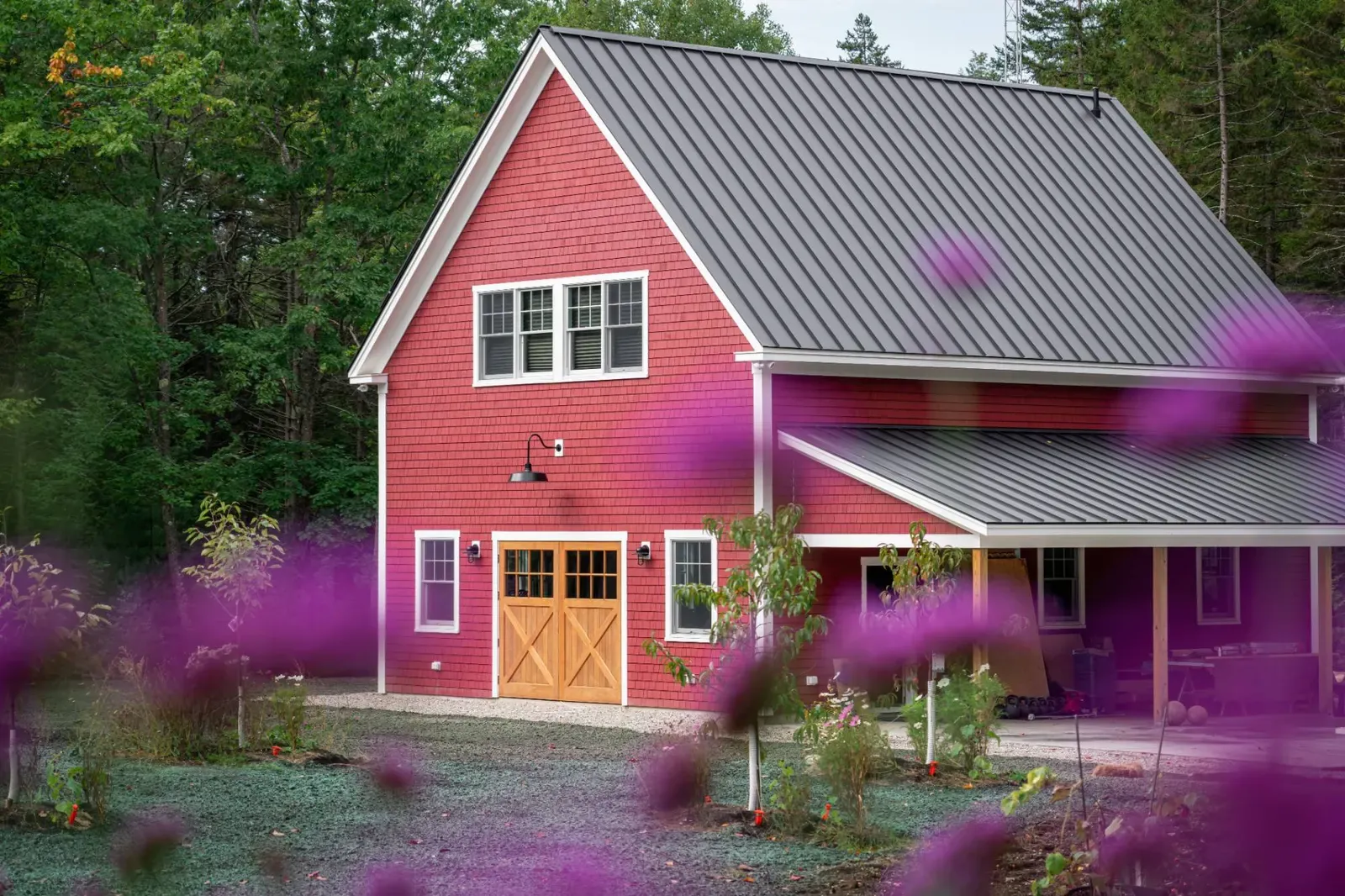 A finished red barndominium home with a black standing-seam metal roof and a covered porch